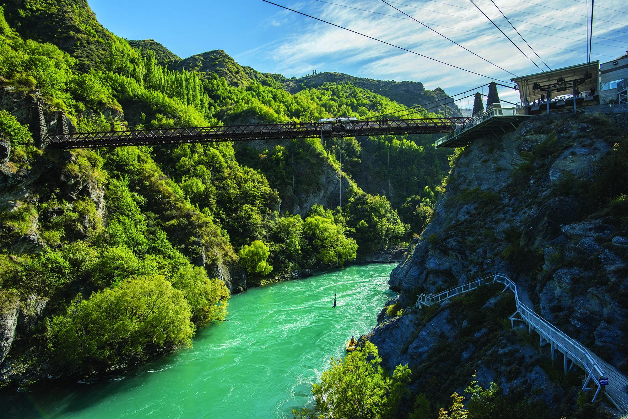 A wide photo of a large red bridge over a deep gorge with bright turquoise water. 