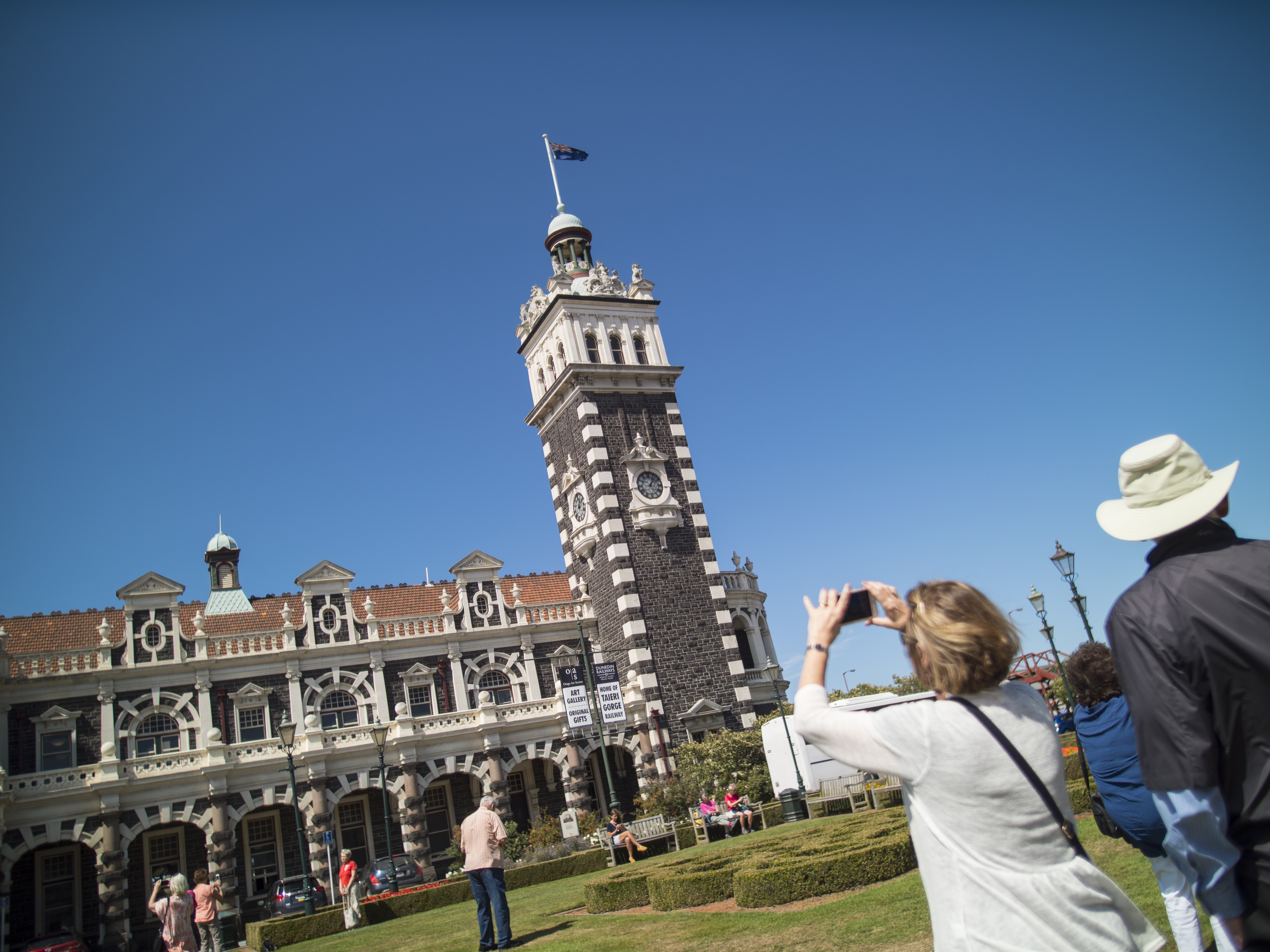 woman taking photo of grand stone building with tower against blue sky