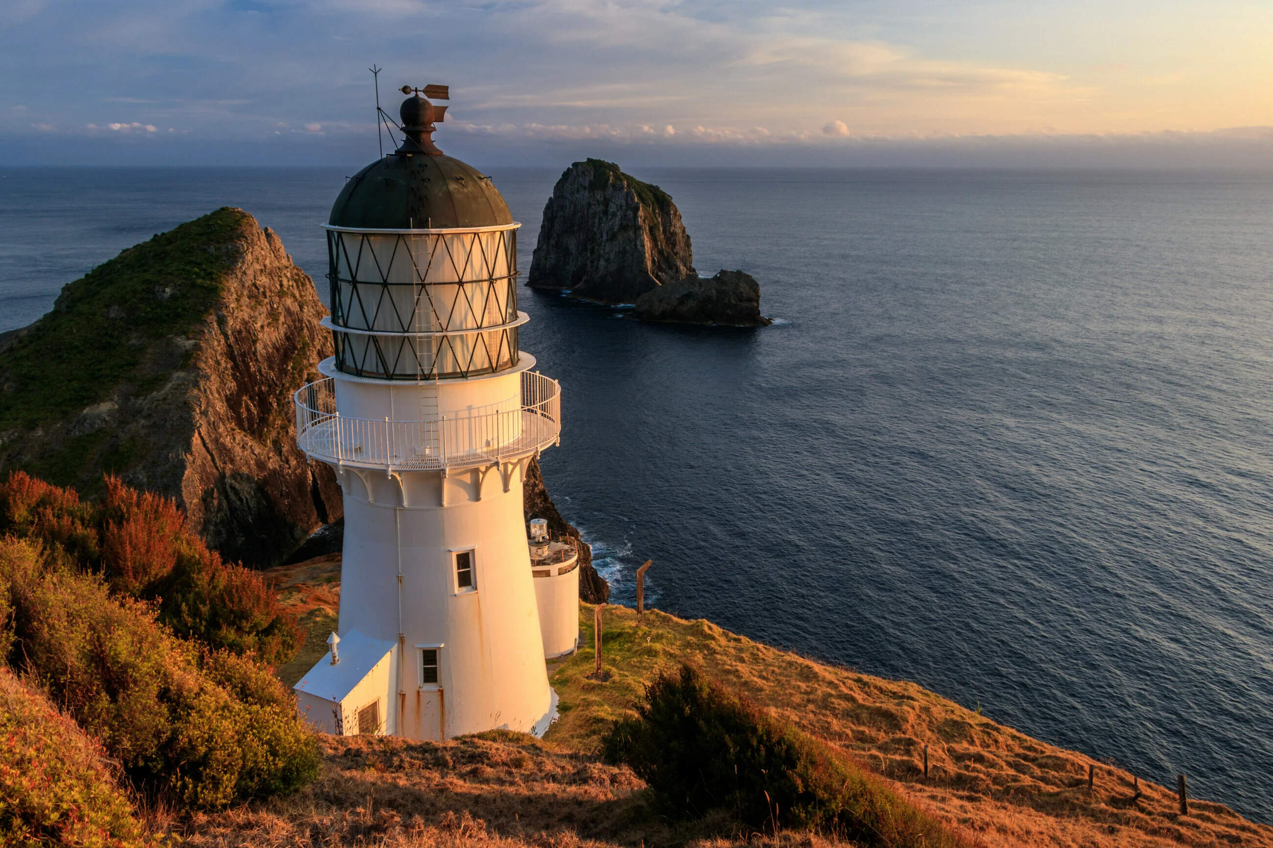 Sunrise light on a lighthouse on a steep cape with ocean off in the distance. 