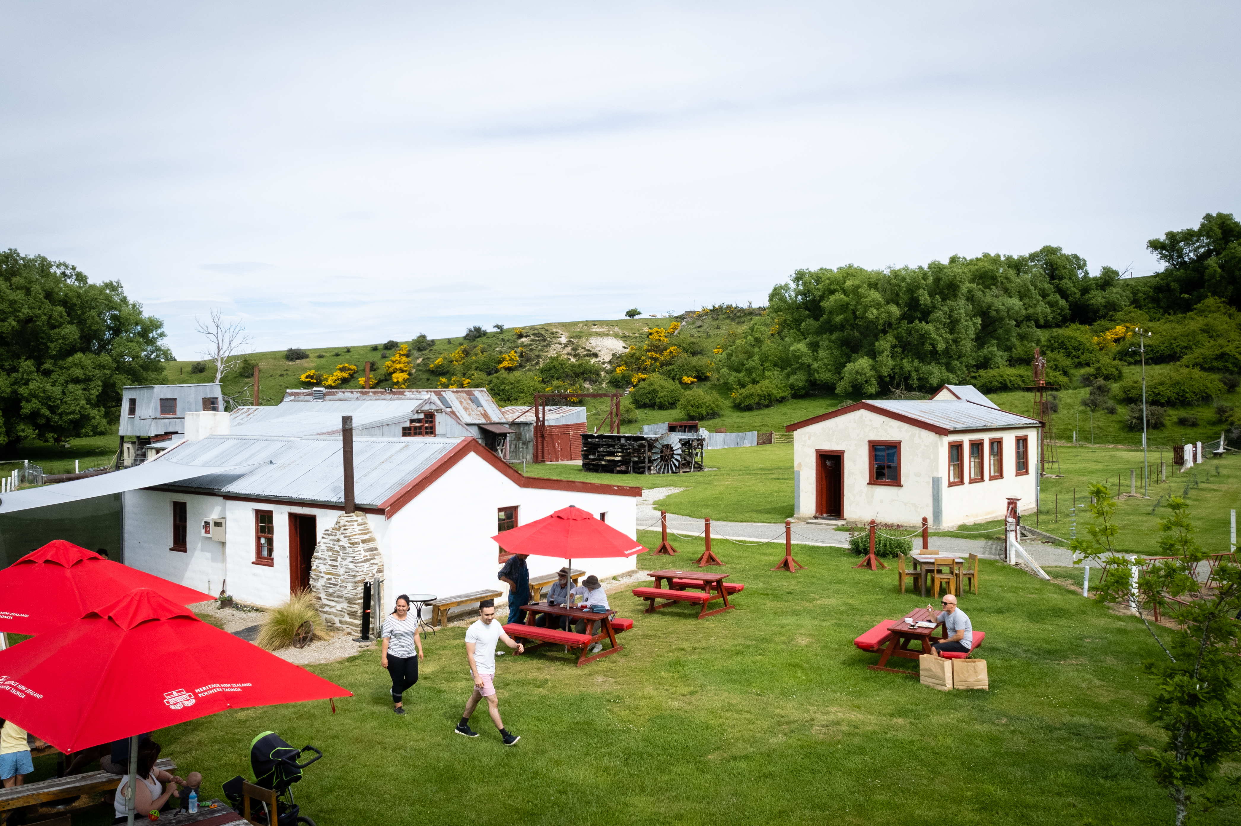 red sun umbrellas and tables in front of green grass and whitewashed stone buildings