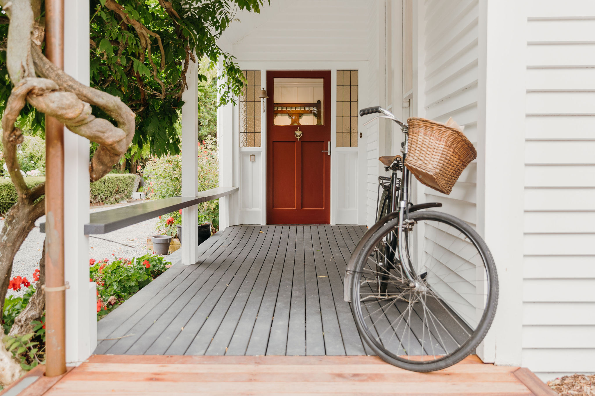 old fashioned bike on verandah of white weatherboard house in front of red door