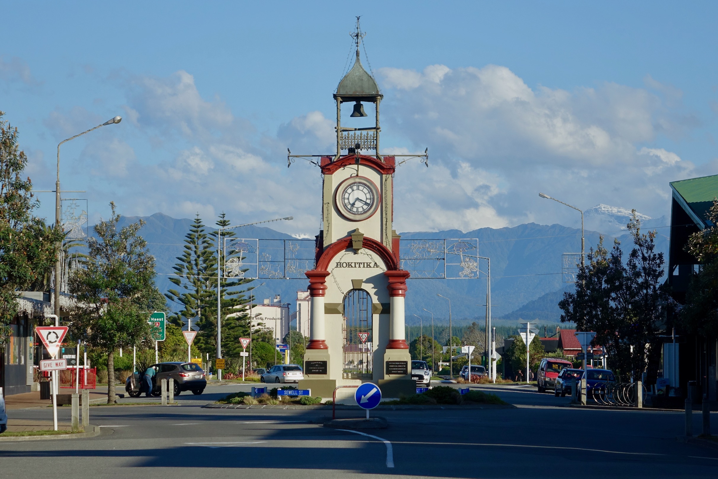 ornate clock tower in middle of street, with hills in background