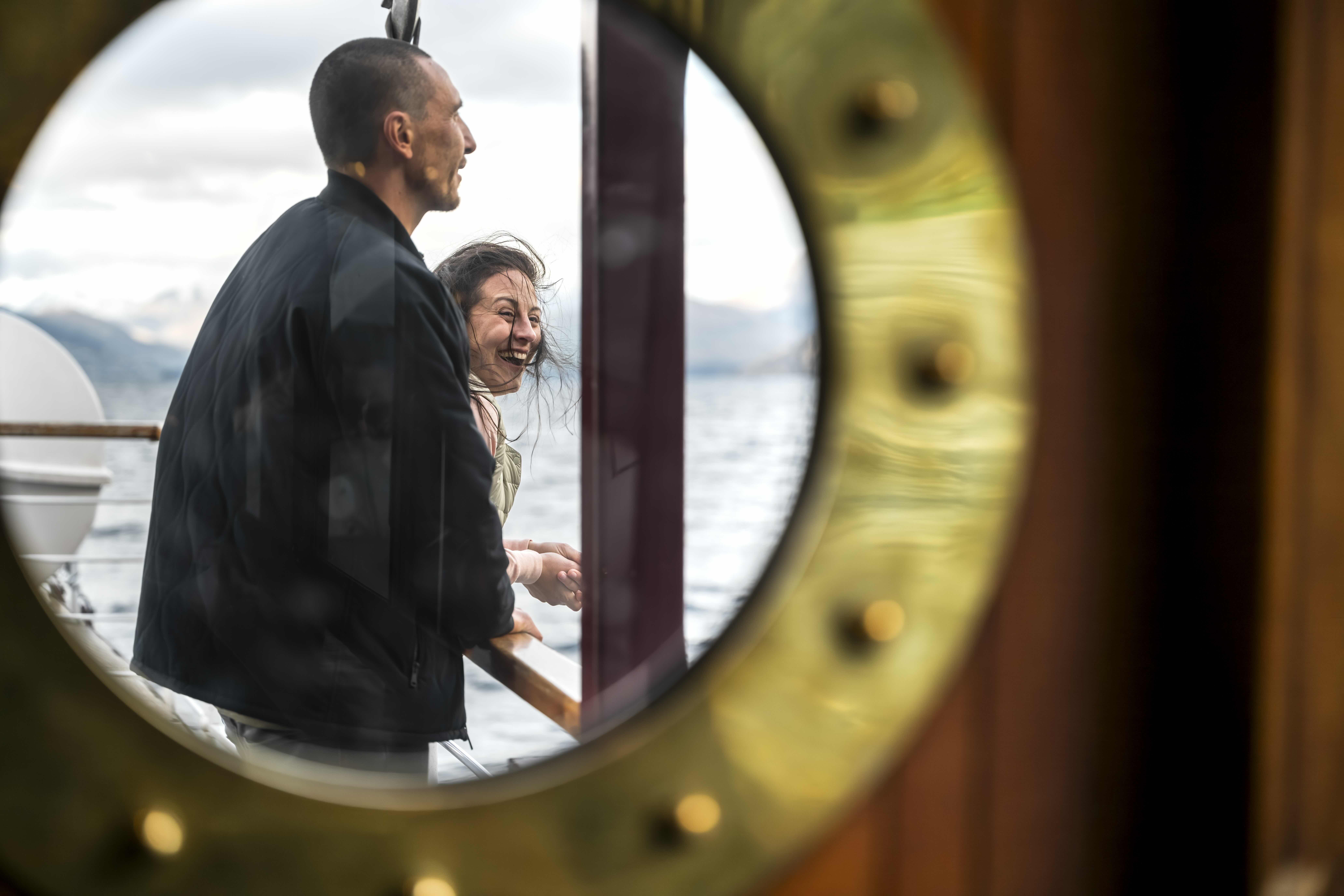 Through a porthole we see a man and woman enjoying the view of the lake. 