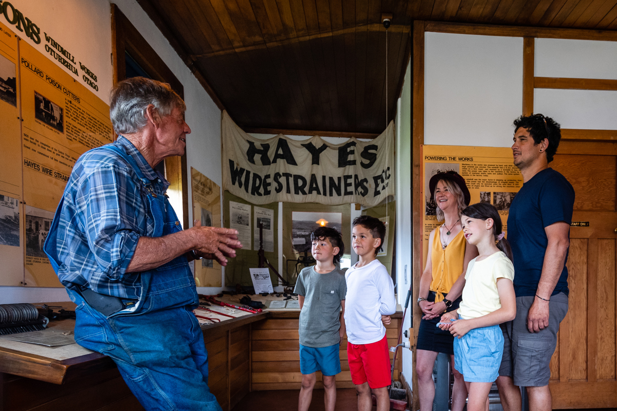Man in dungarees talks to family of parents and three kids about in Hayes Engineering museum