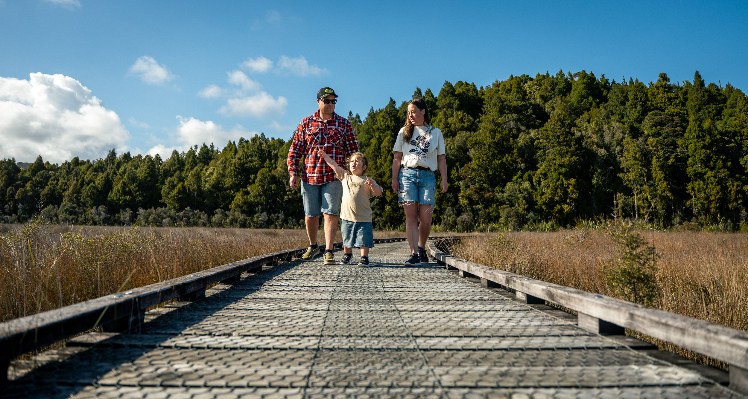 Dad, toddler and Mum on a boardwalk, bush in the background