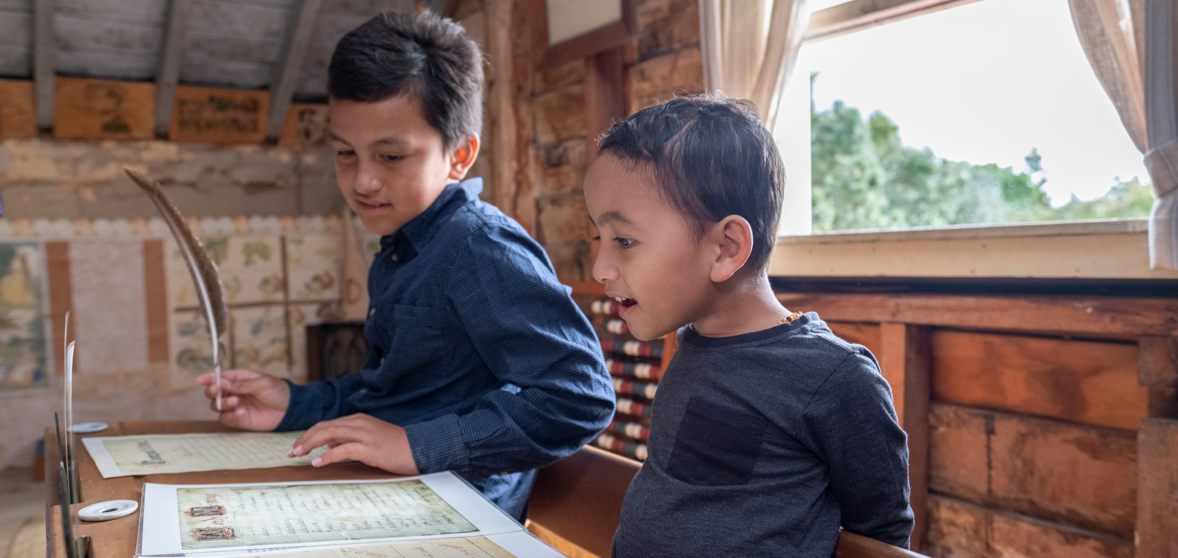 Two young Māori boys looking at documents infront of open window in old house