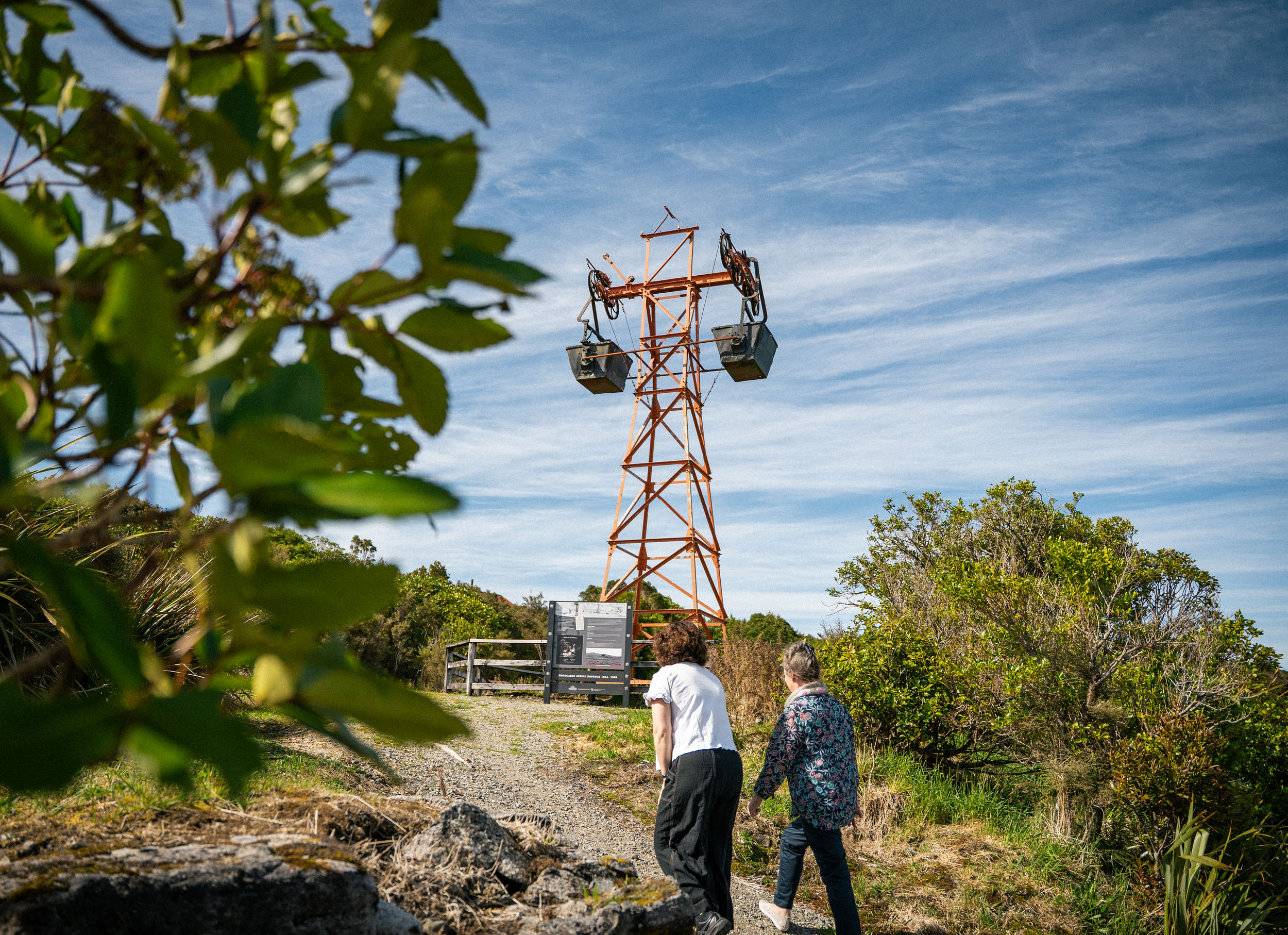 two women walk up hill towards old coal buckets hung on tower