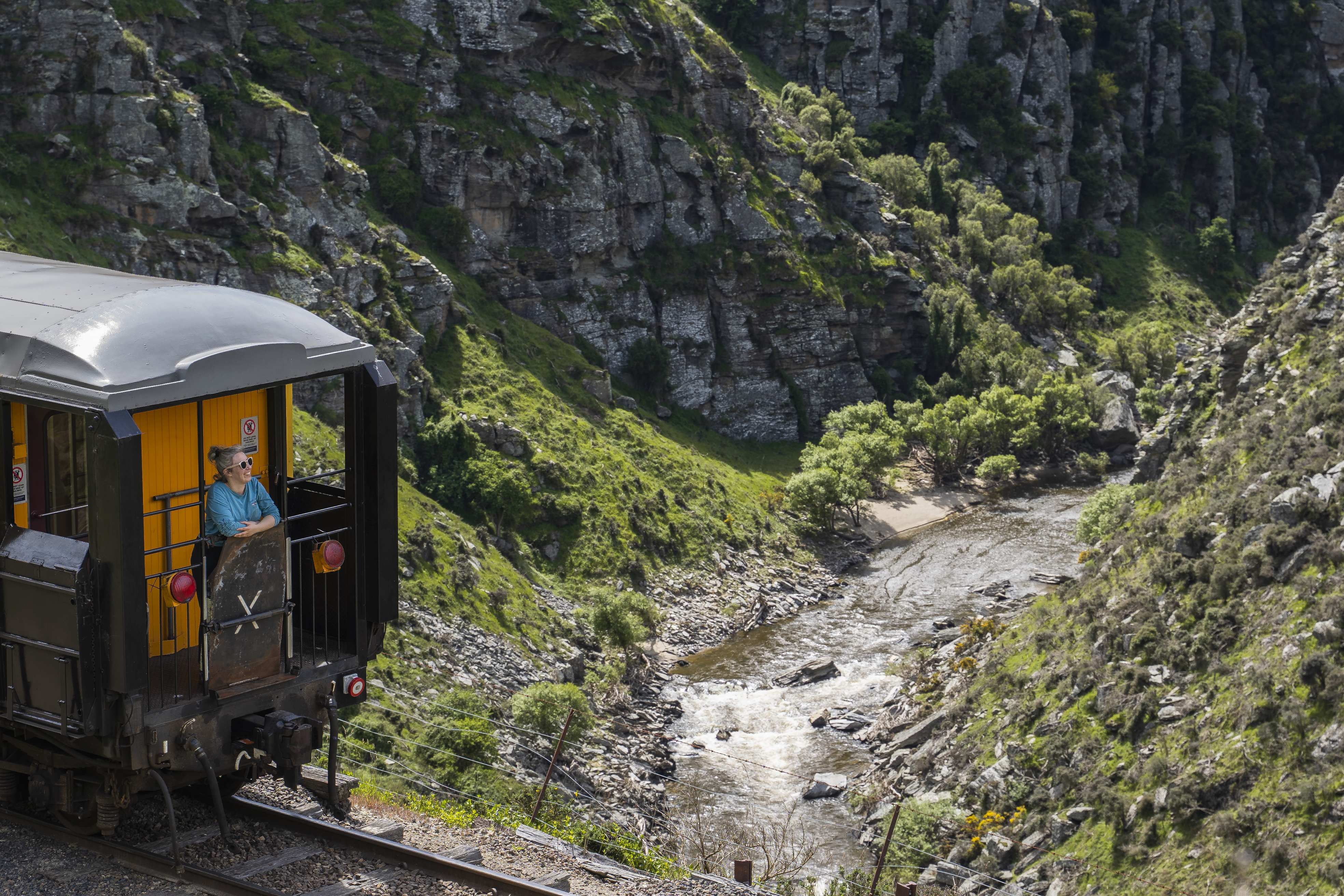 A woman at the end of a train gazes out over the Taieri Gorge.