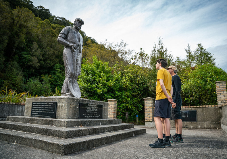 A father and teenage son look up at a statue of a miner at Brunner Mine.