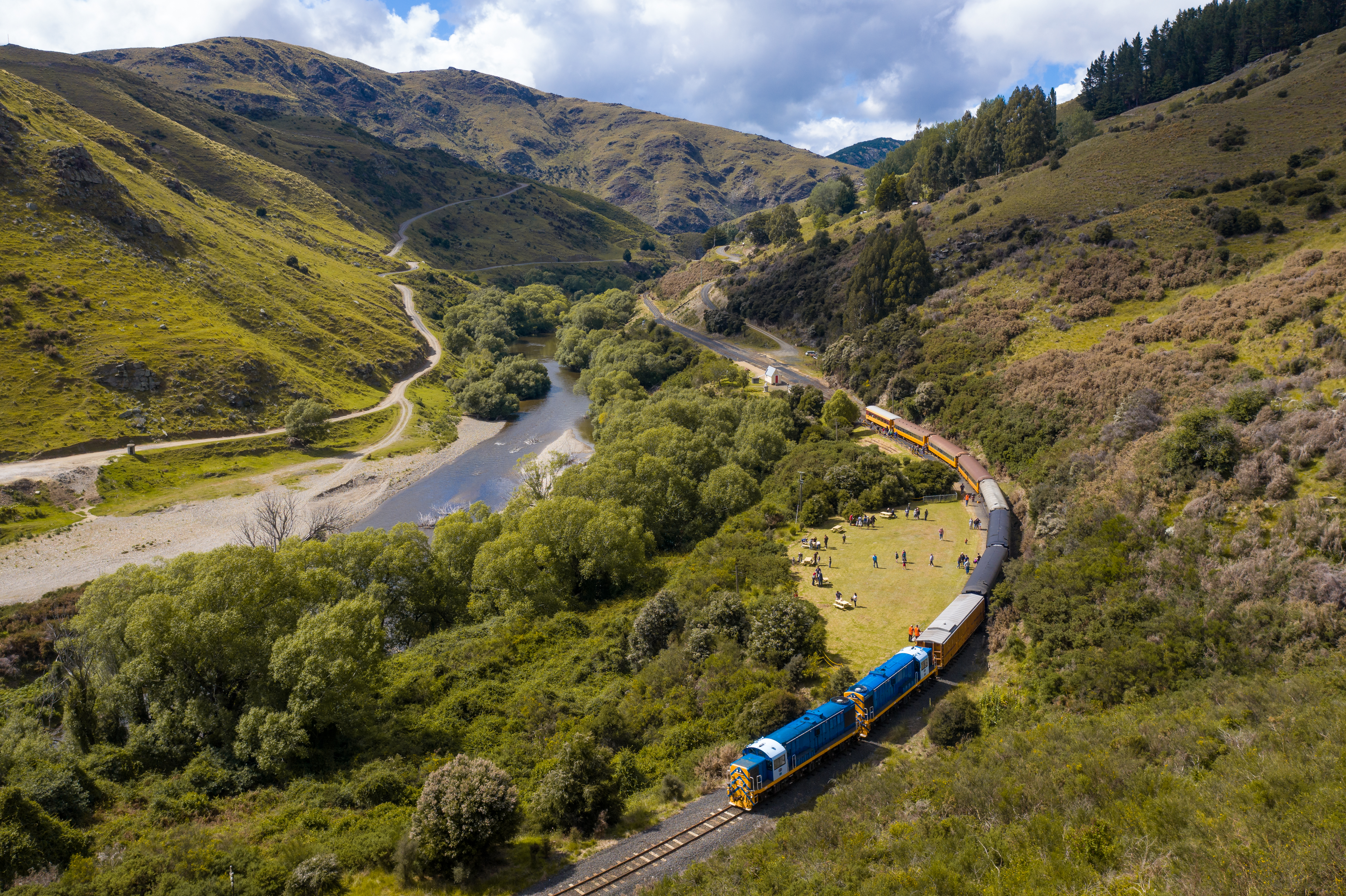 Aerial view of blue and yellow train winding through mountain scenery