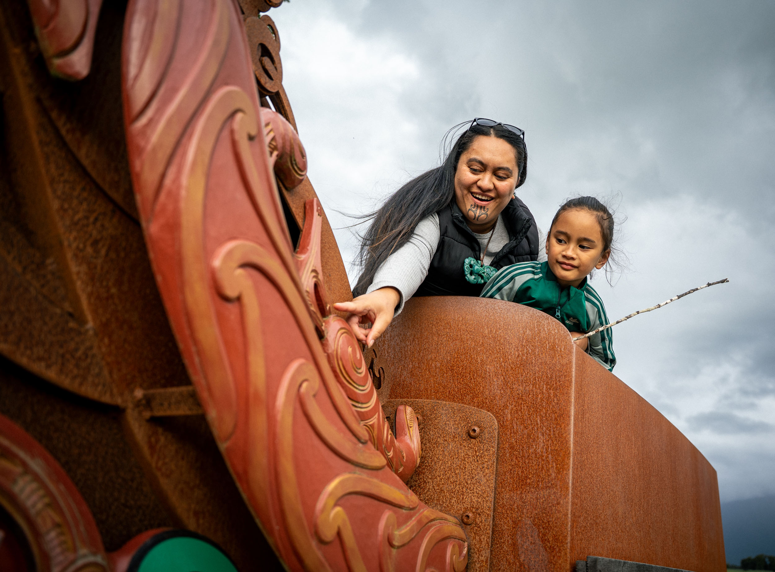woman and boy on carved waka sculpture