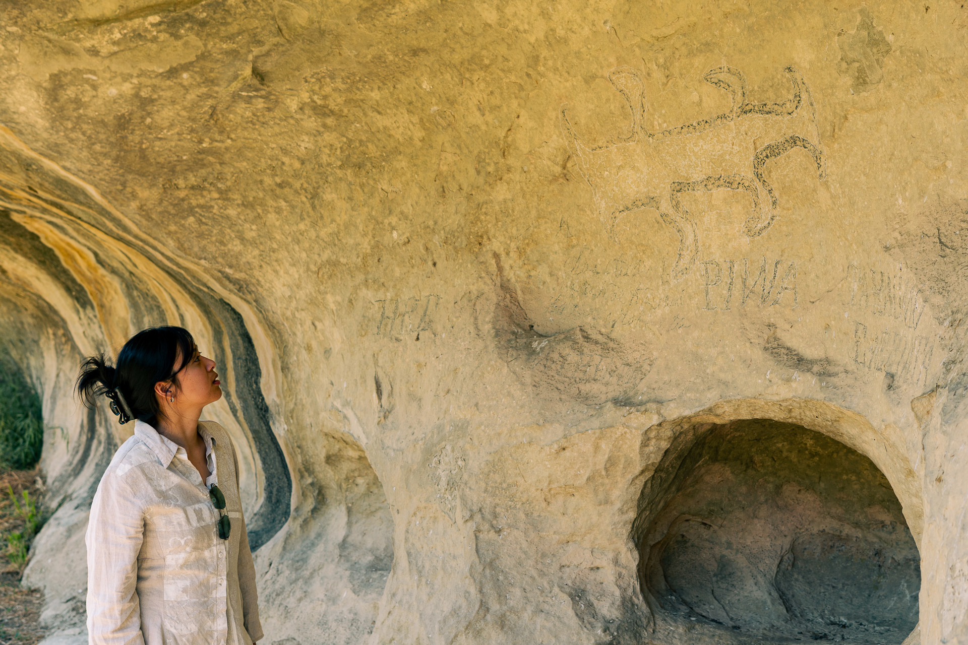 A young Asian woman looks at limestone caves with paintings on the rockface.