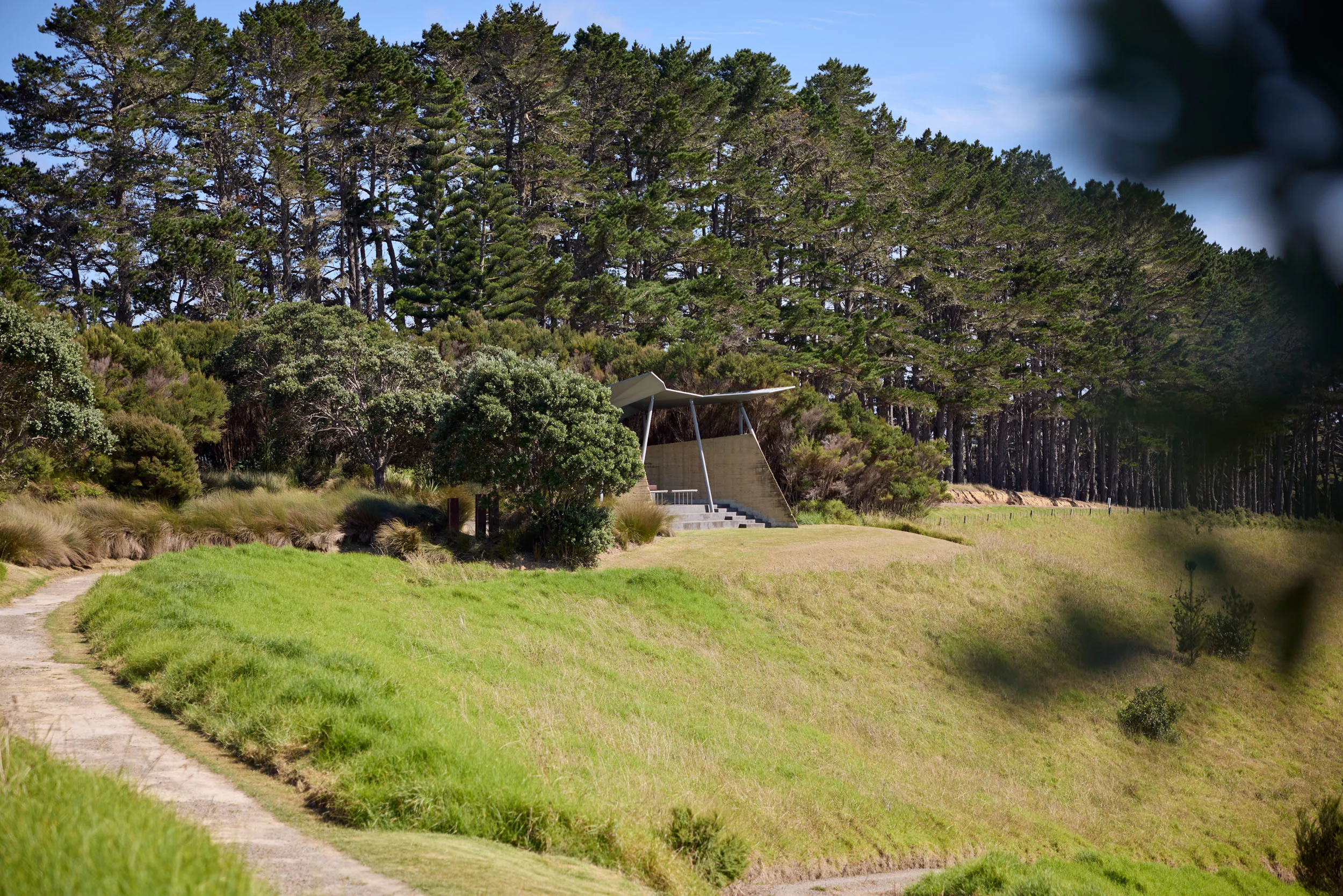 Wide landscape of green hillside with architectural shelter at Rangihoua. 