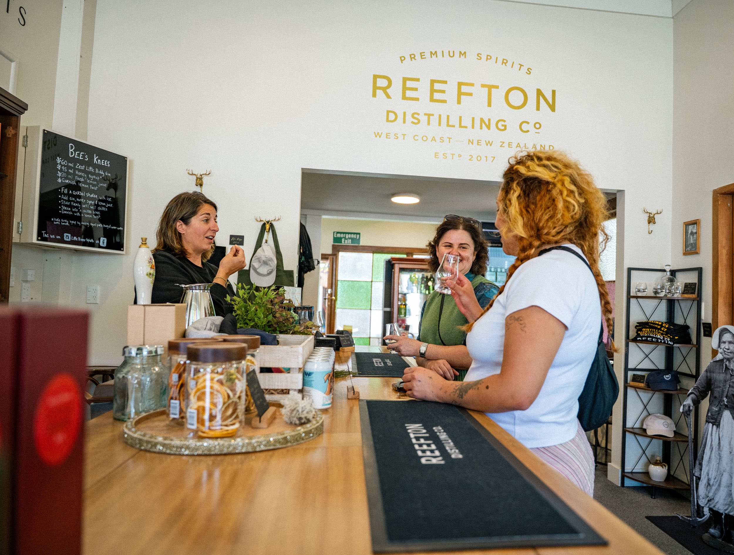 Three women drinking from small glasses in distillery shop