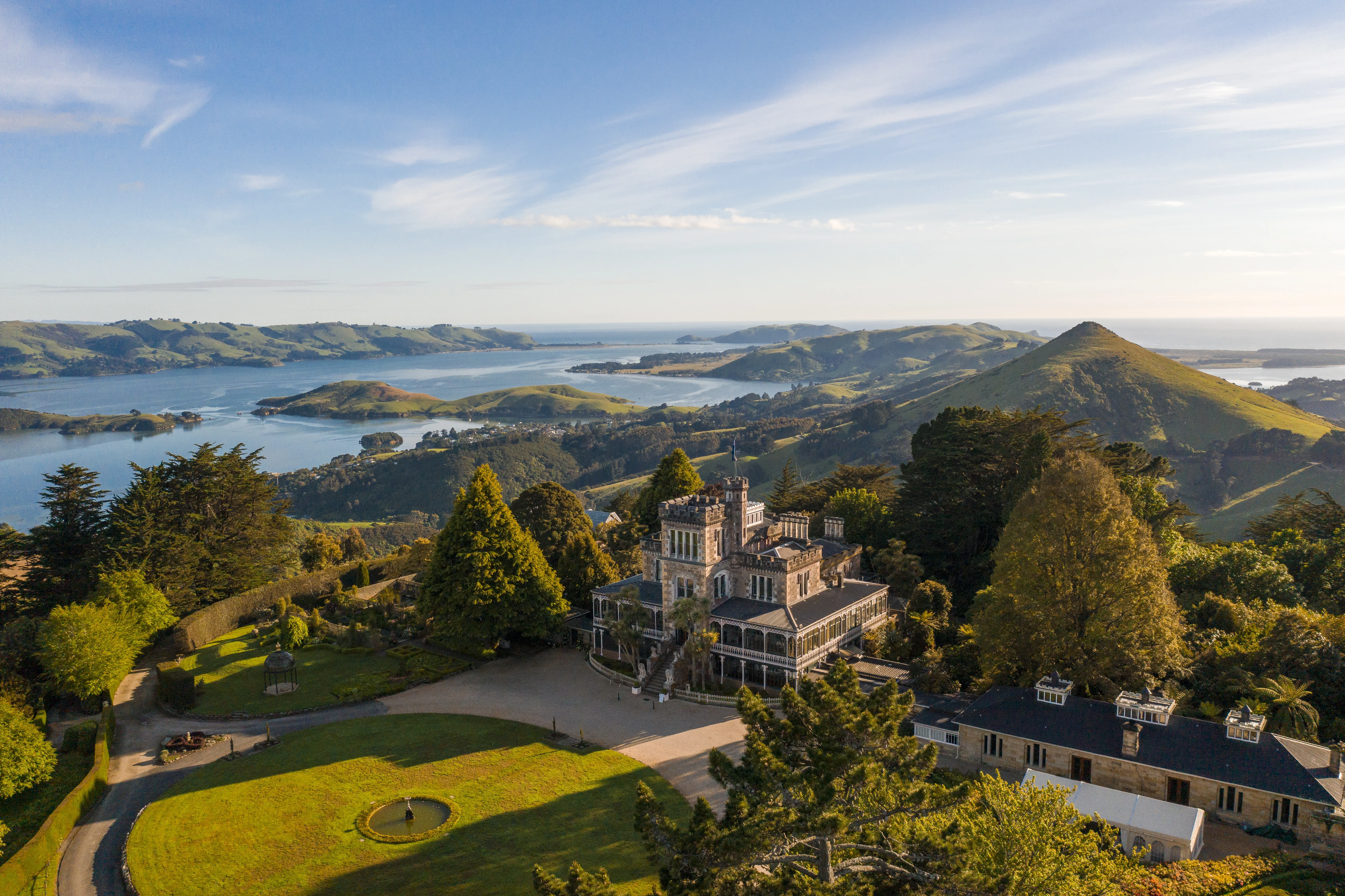 Wide shot from above of grand Larnach Castle with beautiful green Otago Peninsula stretching out behind. 