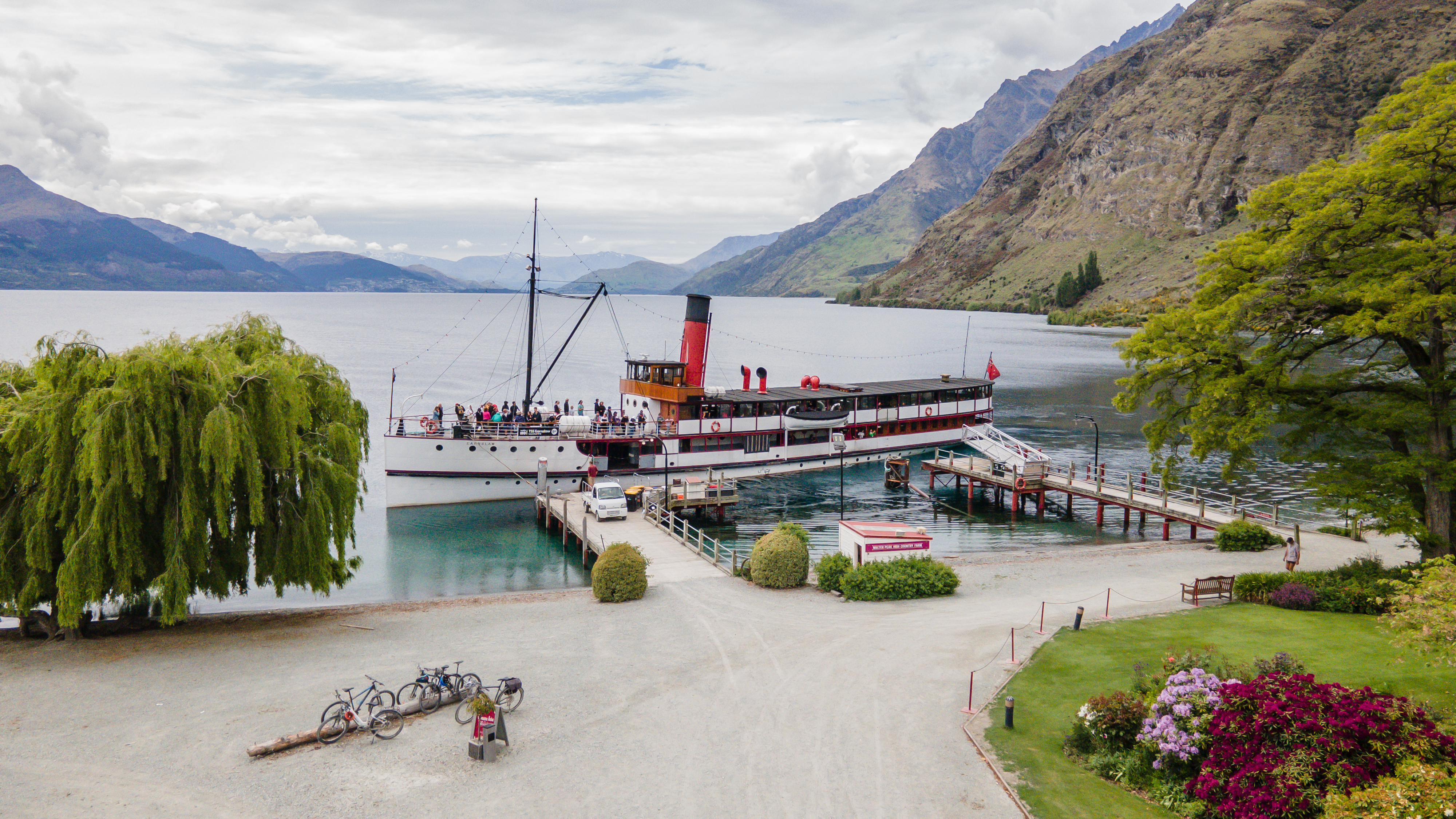 Historic steamship docked at lake, surrounded by mountains, blue sky, sun shining, bikes in foreground