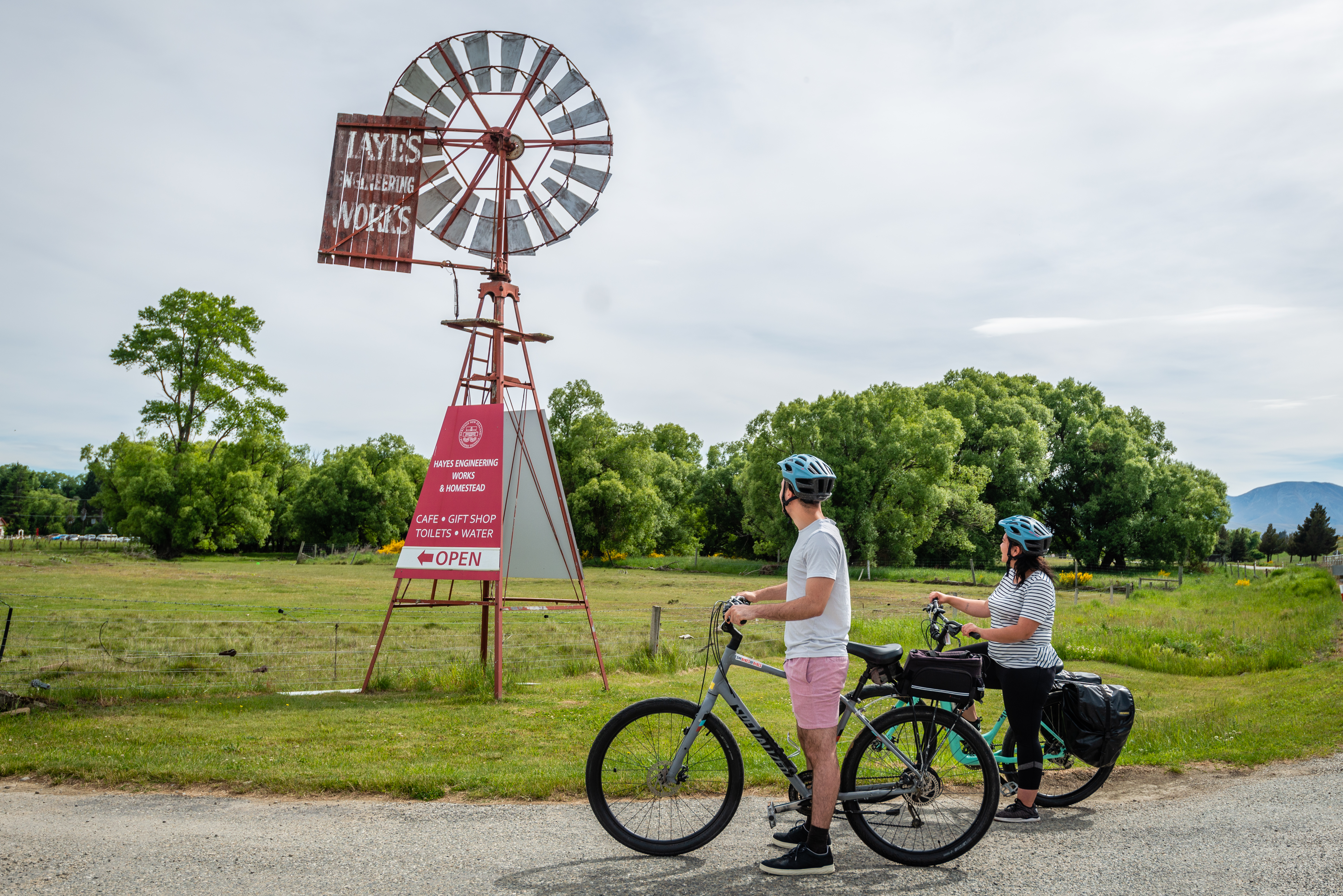 Two people on bikes have stopped to look up at the Historic Hayes sign and windmill.