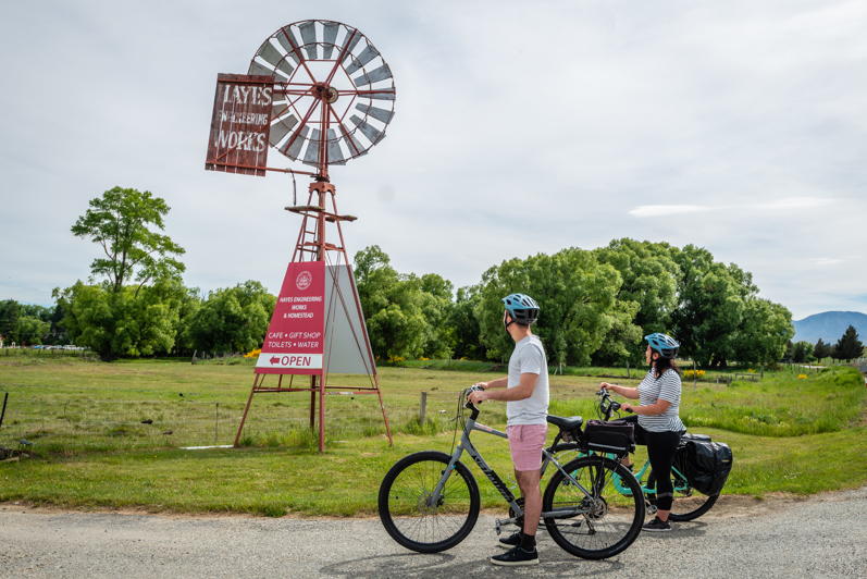 Two people on bikes have stopped to look up at the Historic Hayes sign and windmill.