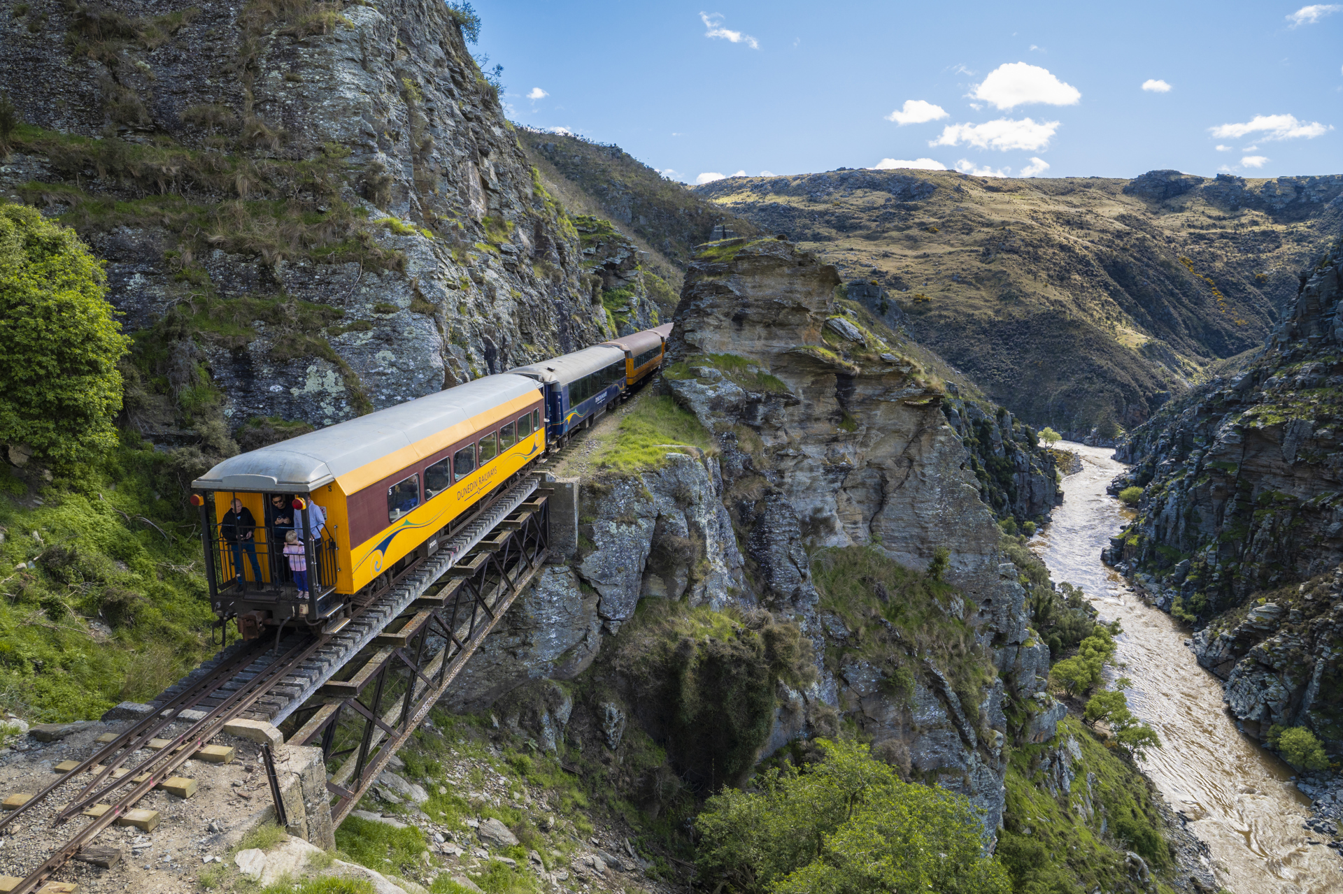 A yellow train running along side a large gorge. 