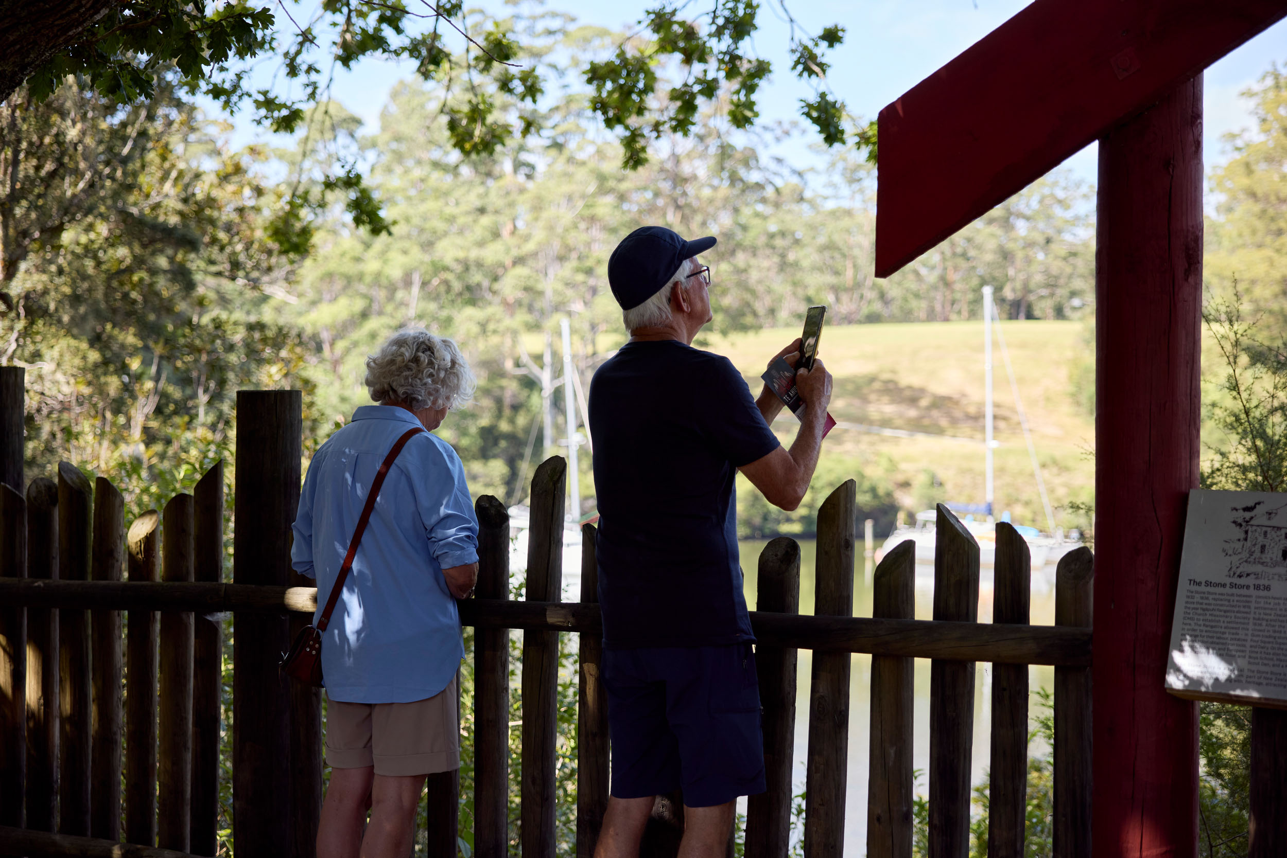 older man and women taking photo from behind fence of view over harbour