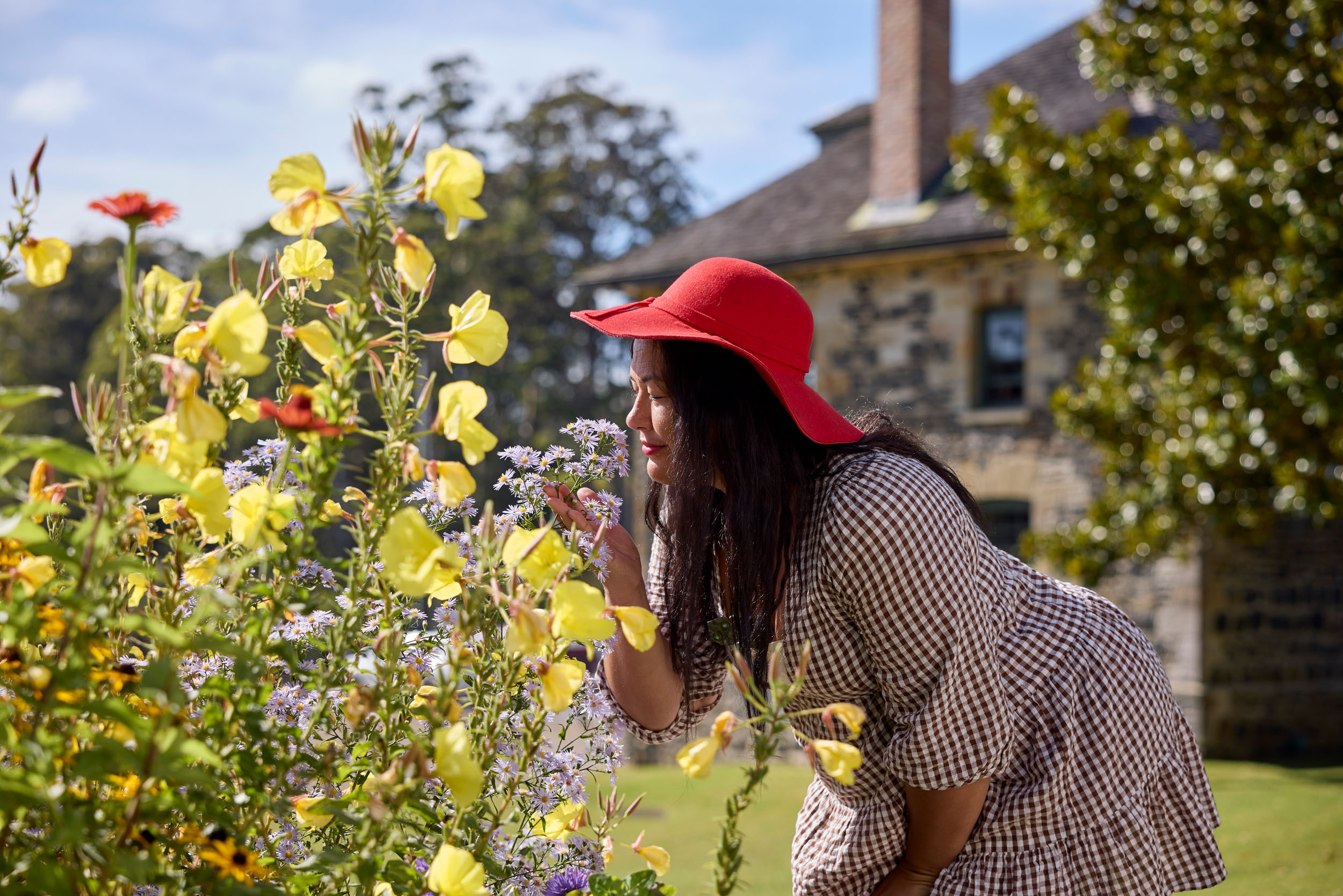 woman in red hat smells yellow flowers