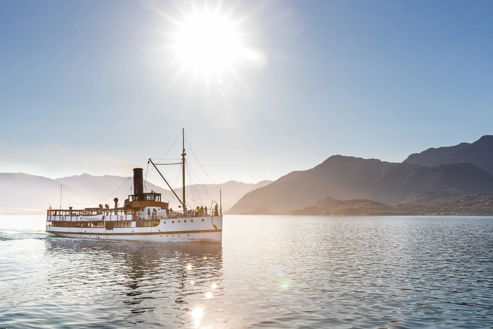 An old steam boat on a placid lake with craggy mountains behind, sunny day with blue sky. 