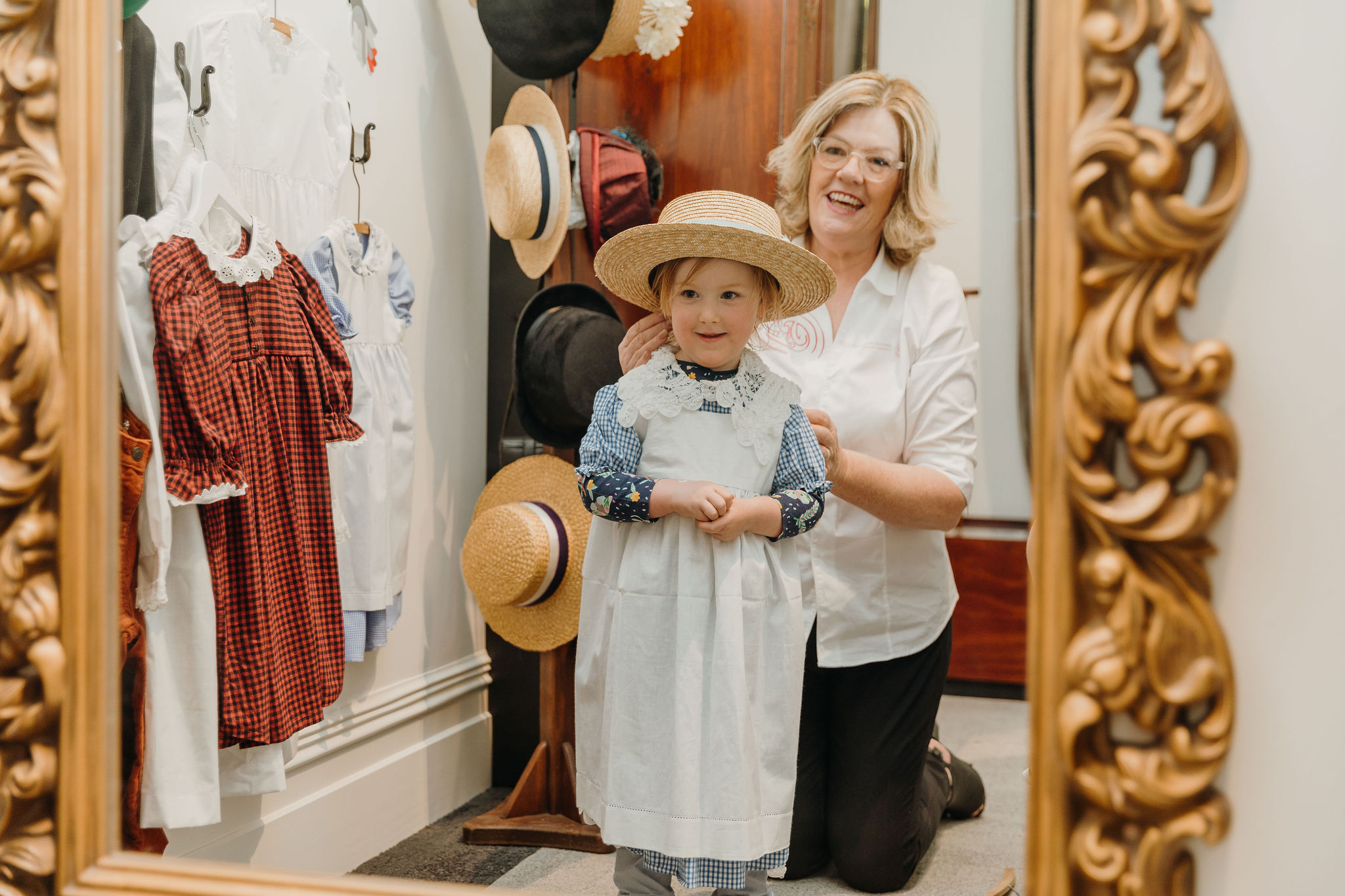 small girl dressed up in Victorian dress and hat with lady behind