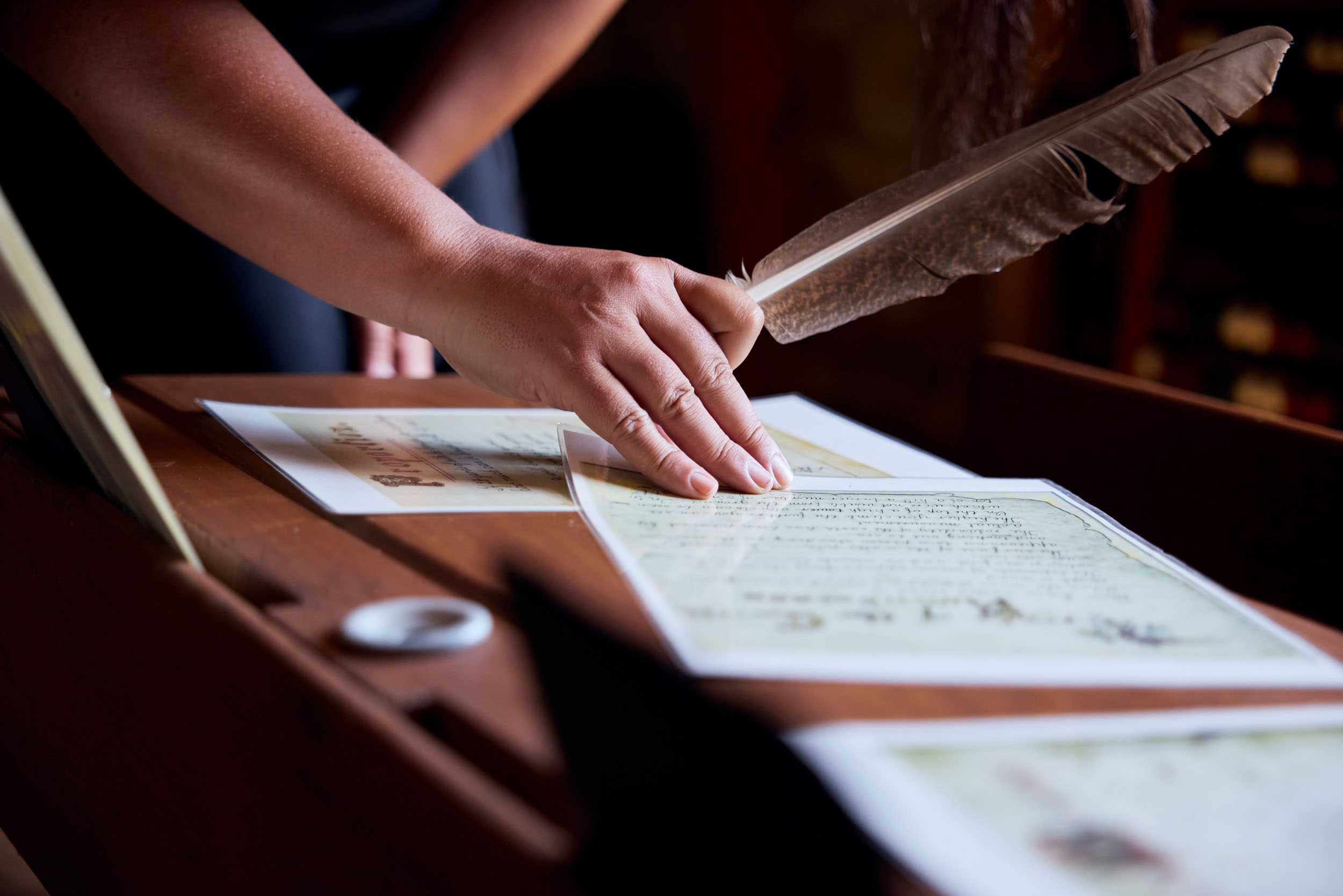 hand holding feather quill touching documents on a desk